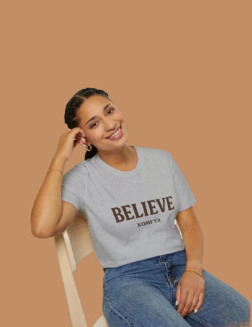 Woman wearing a gray t-shirt with 'BELIEVE' printed on it, sitting on a white chair.